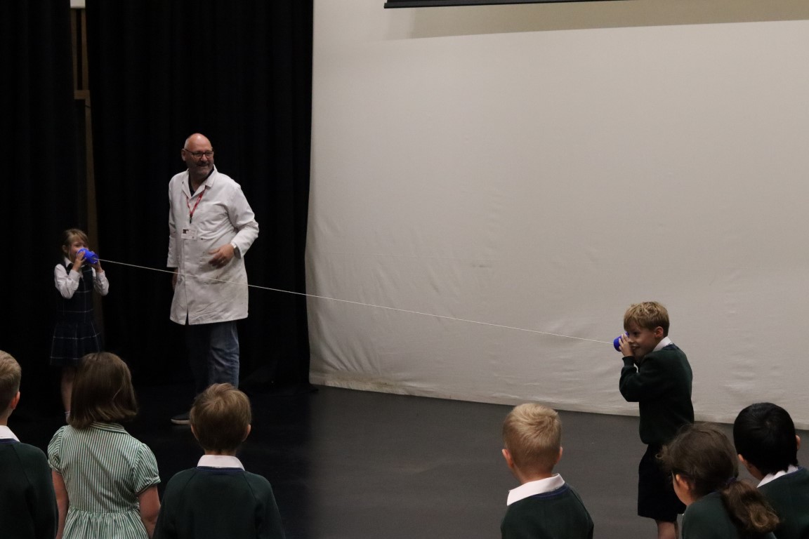 two children listen to each other through plastic cups and string during a sound experiement