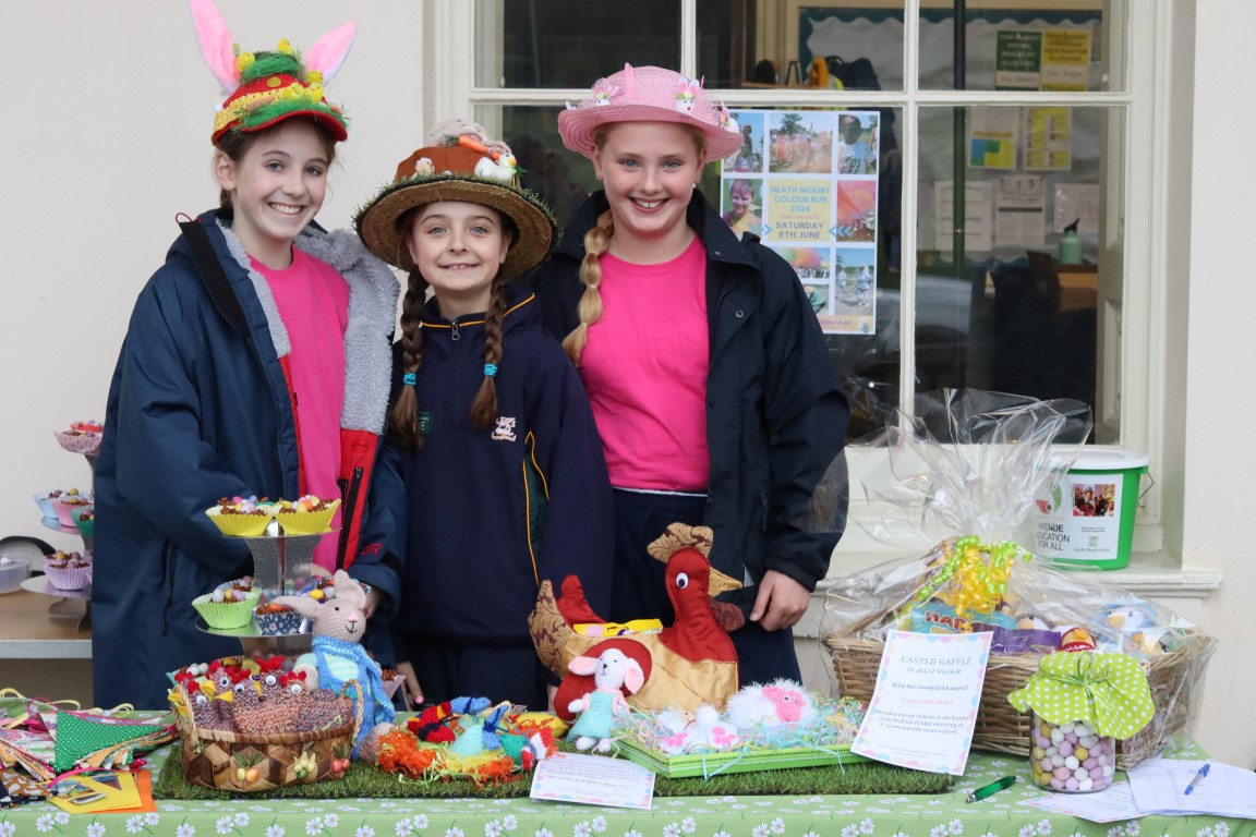 Three pupils stand behind their charity craft stall selling cakes, knitted decorations and bunting
