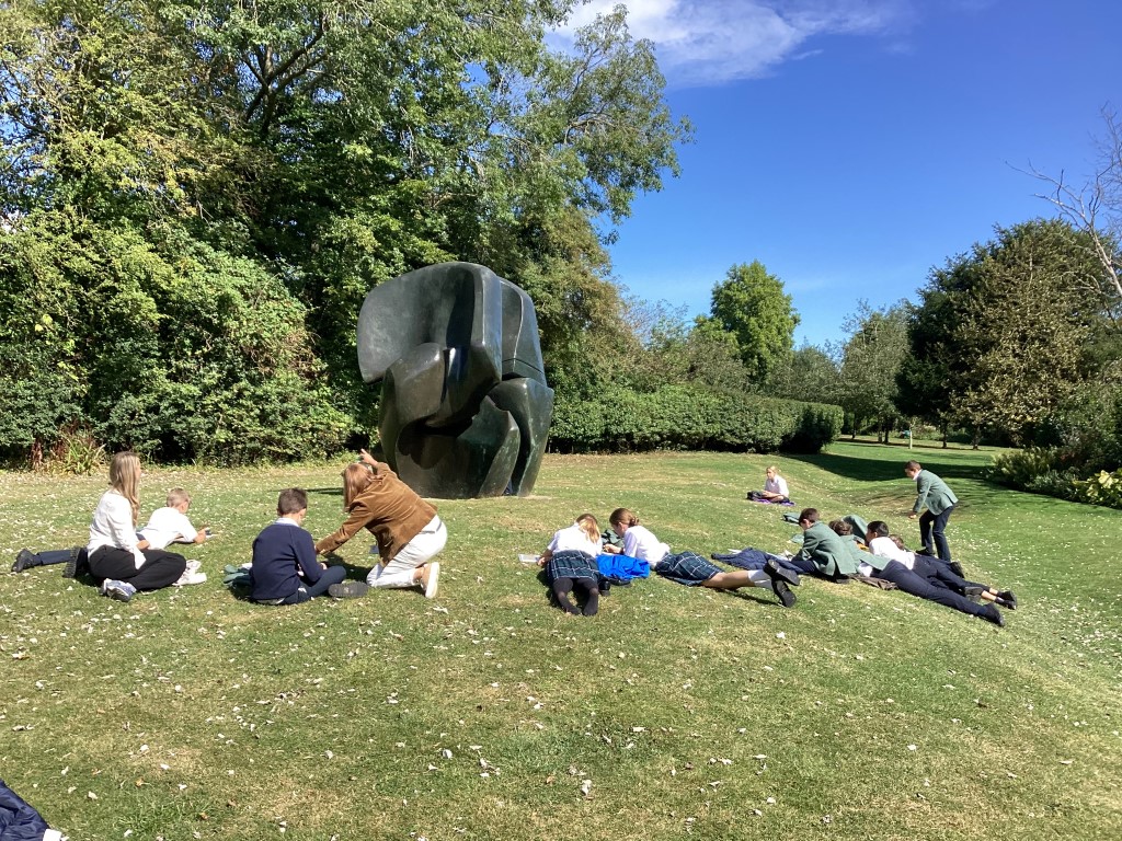 pupils lie on the grass in the sunshine sketching a Henry Moore sculpture